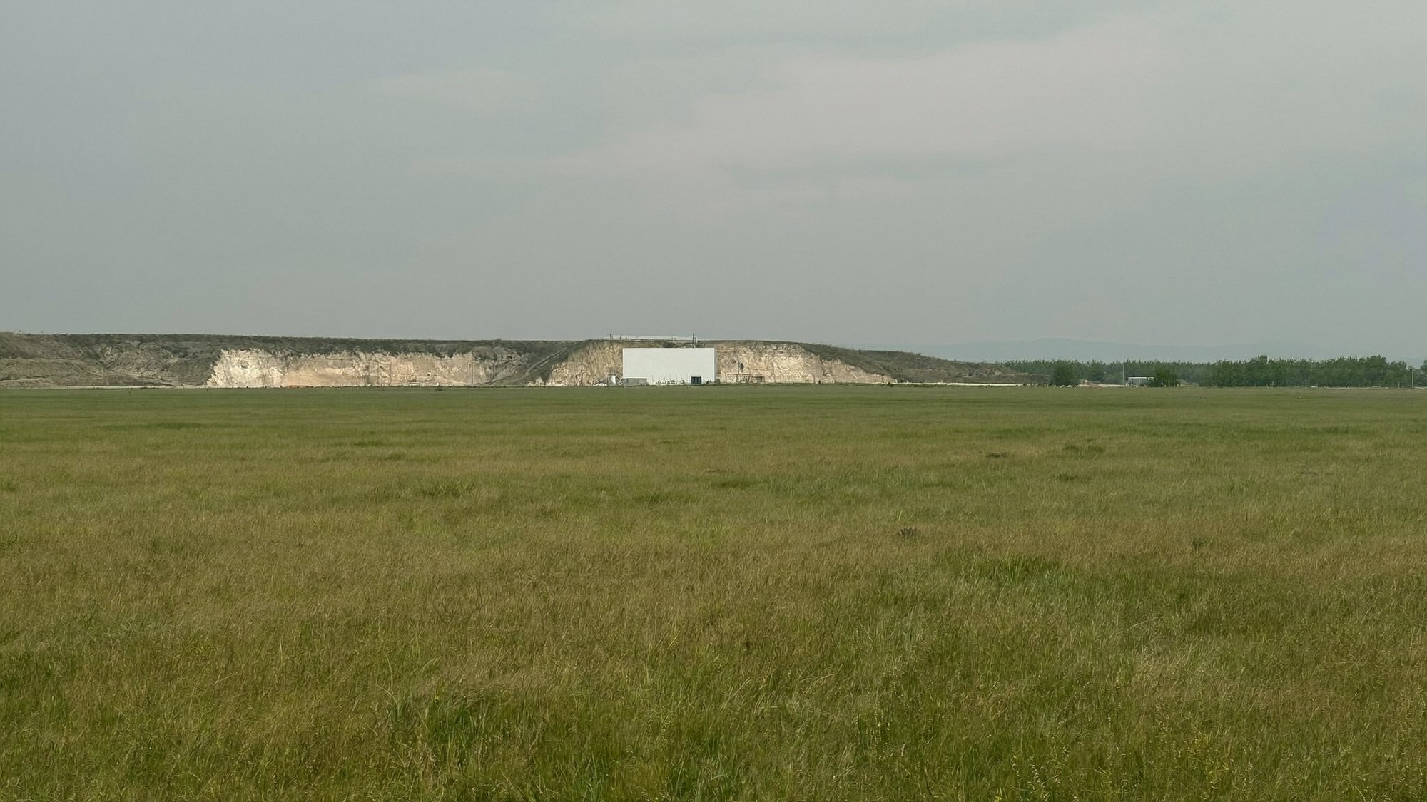 Empty grass foreground filling the frame with a small quarry on the distant horizon