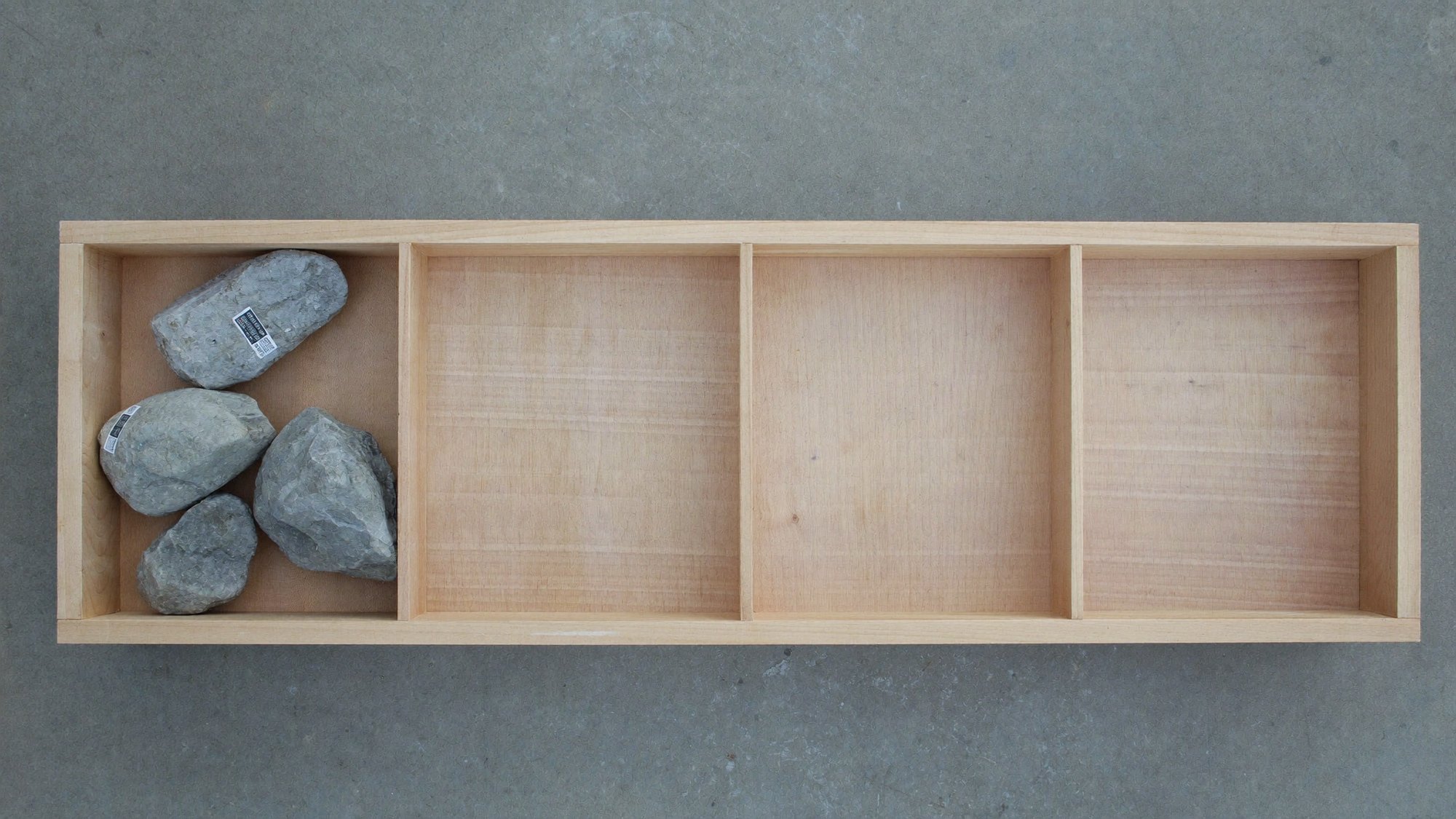 Overhead view of a bare timber core tray with one compartment holding rock and three empty