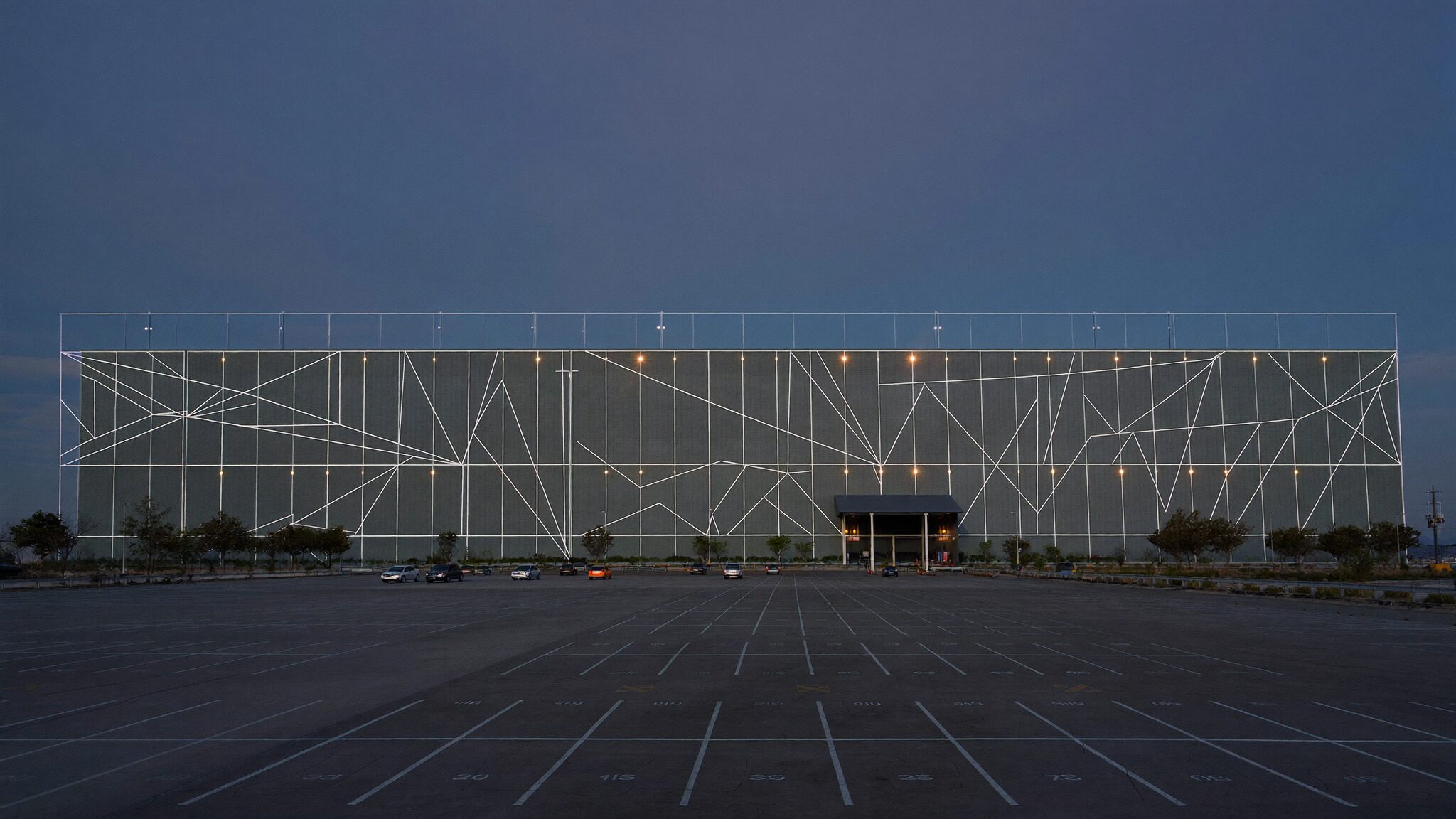 Vast empty parking lot at dawn in front of a windowless hyperscale data-center building, only four cars parked
