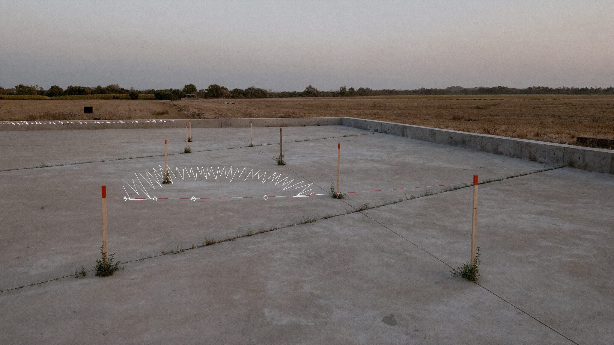 Empty concrete slab with survey stakes and weeds growing in the joints