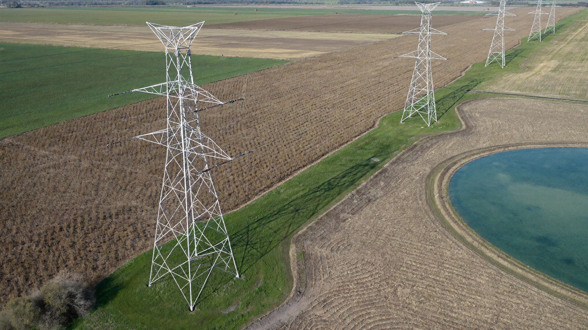Aerial view of a transmission line crossing row-crop fields beside an irrigation pond