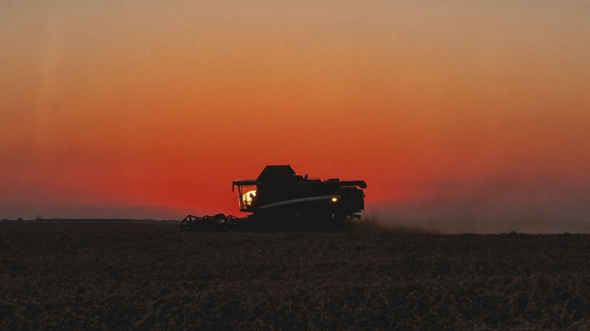 A combine silhouetted against an orange sunset during harvest
