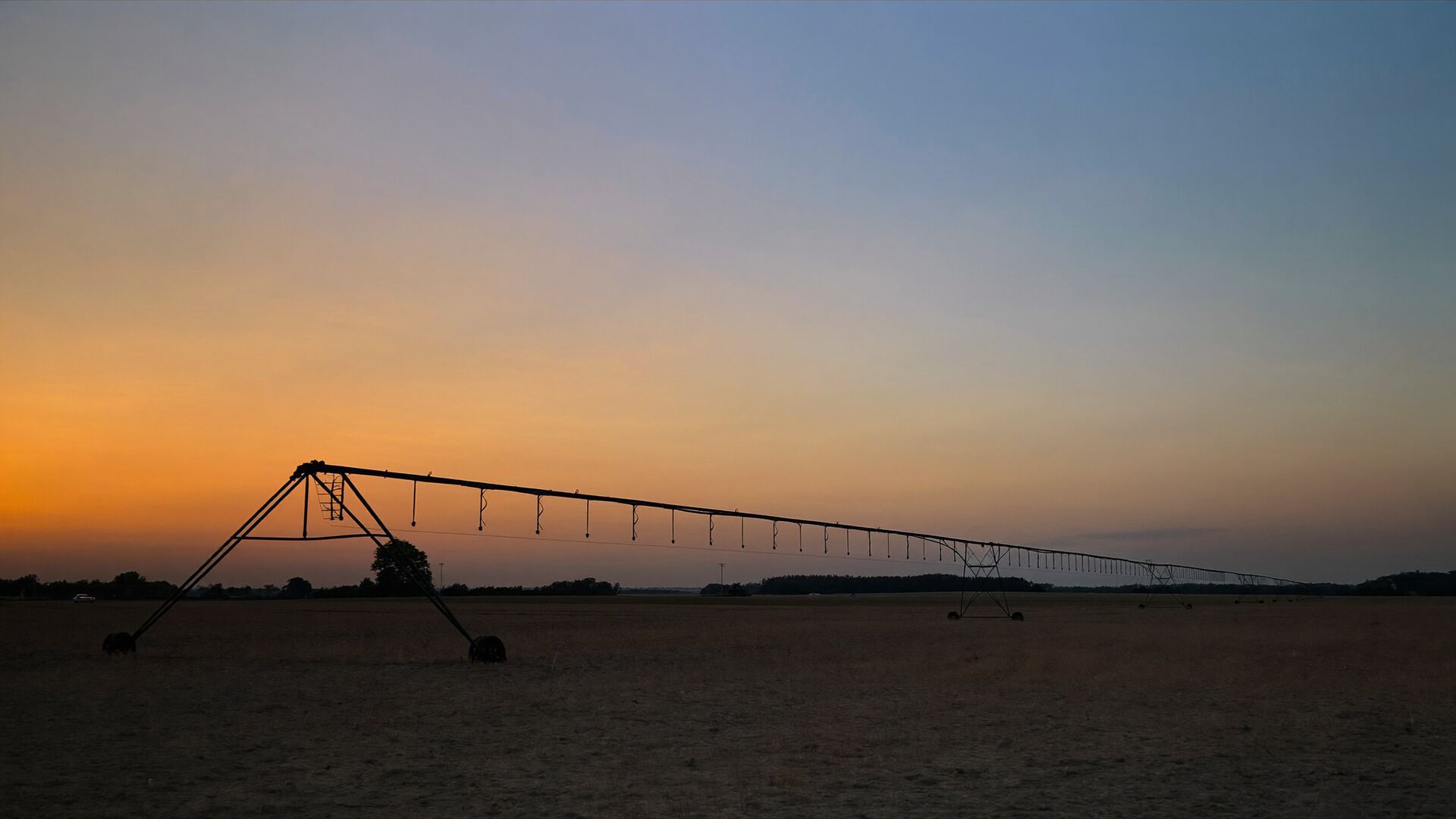 A center-pivot irrigation system silhouetted across a field at dusk
