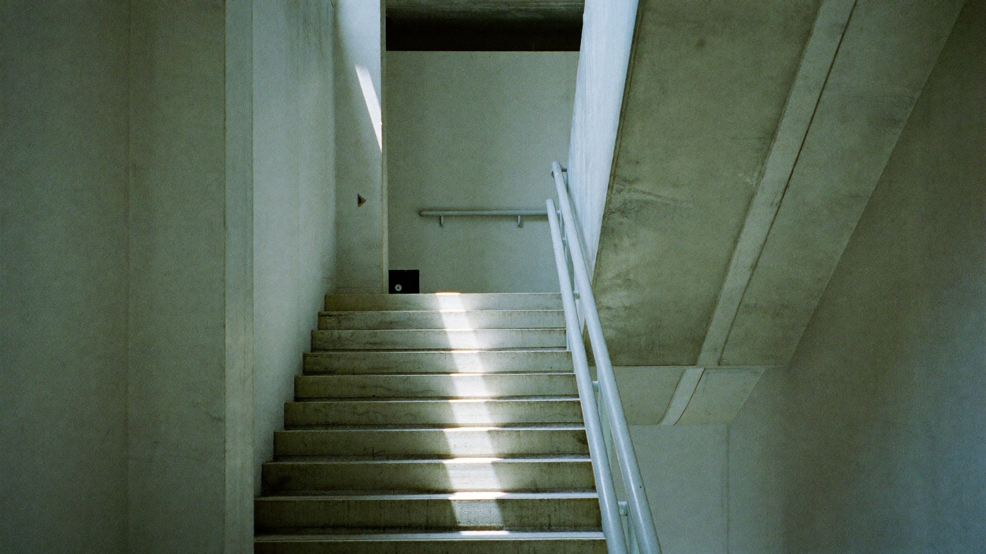 A bare concrete stairwell lit by a single shaft of daylight