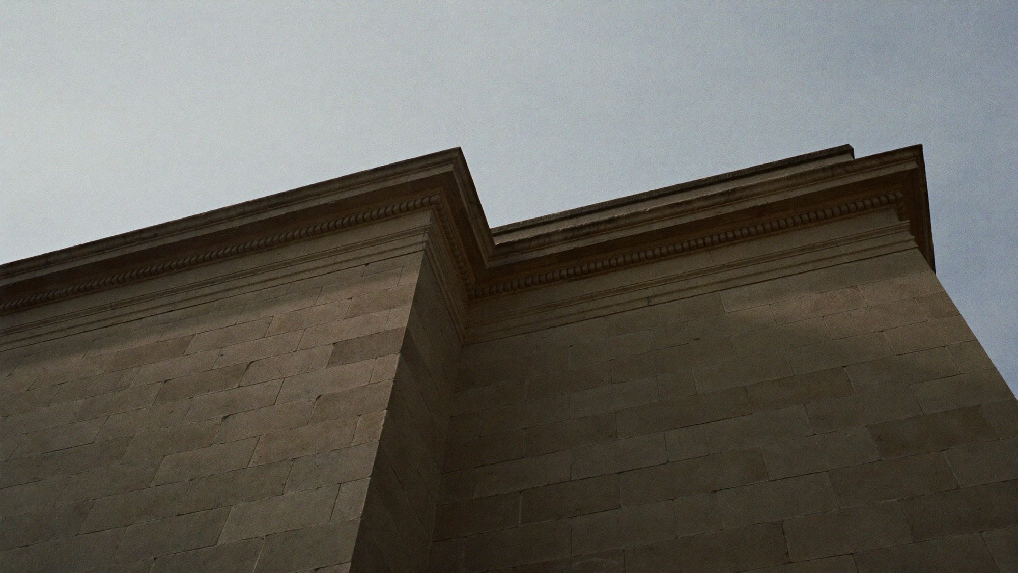 The corner of a stone building shot steeply from below against a pale sky