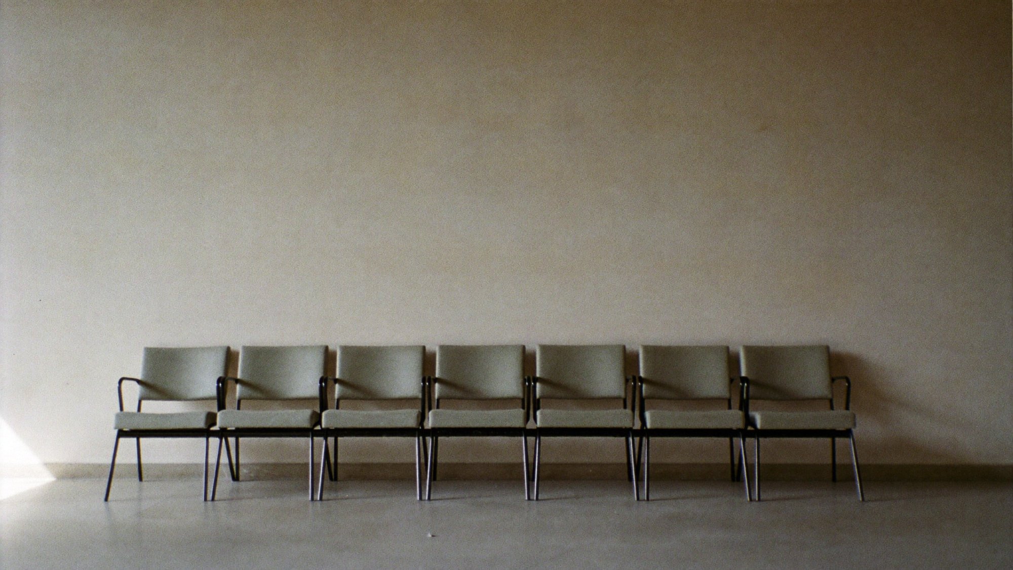 A row of empty waiting-room chairs against a blank wall