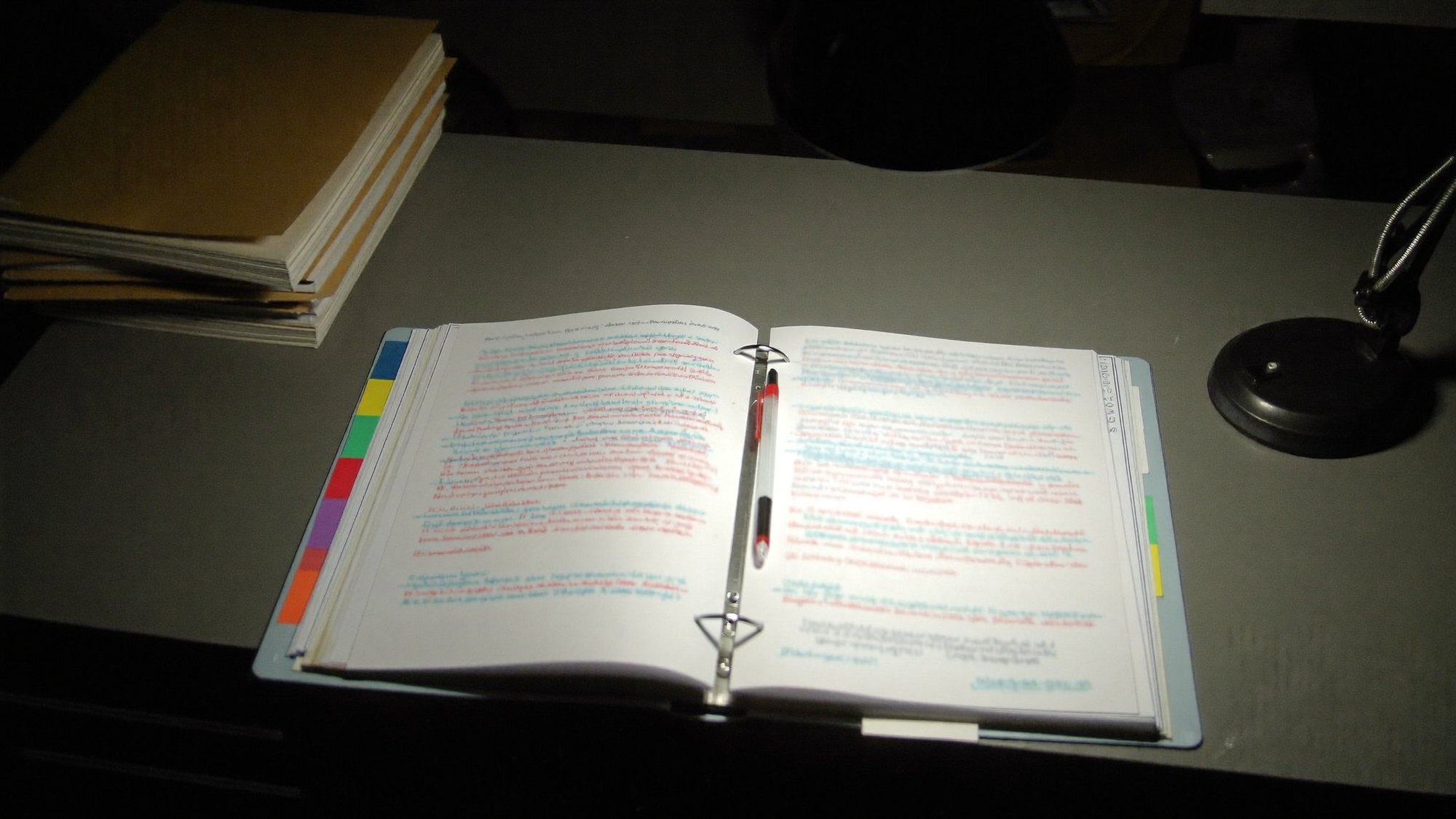A tabbed binder open on a desk with a red pen resting across the page